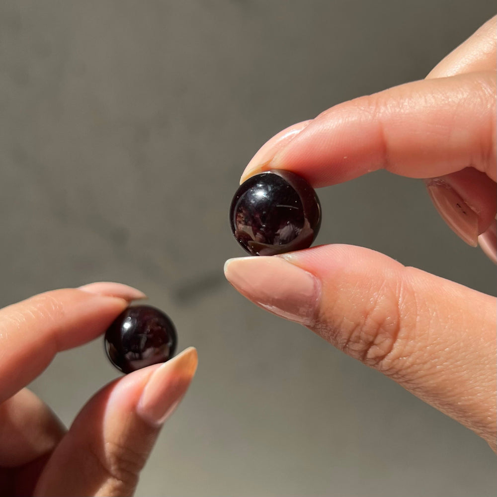 Two hands holding a pair of meditation harmoniser almandine garnet spheres against a neutral background
