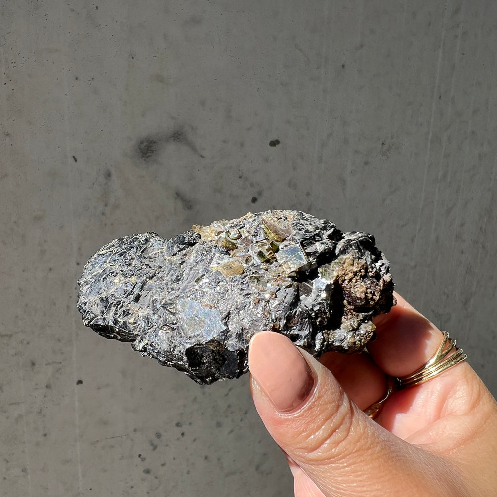hand holding an australian epidote and albite mineral specimen against a grey background