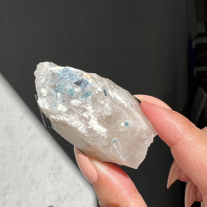 Hand holding a rough indigo tourmaline in quartz against a dark background