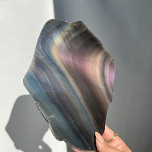 rainbow obsidian slab/slice held by a hand against a neutral background