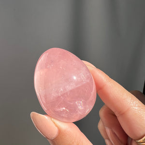 Hand holding a brazilian Rose Quartz polished freeform against a gray background