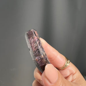 Hexagonal polished star ruby crystal from india held by a hand against a gray background