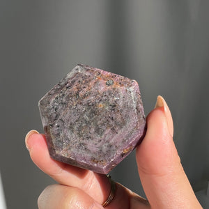 Hexagonal purple polished star ruby crystal from india held by a hand against a gray background