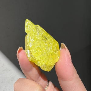 Hand holding a yellow sulphur crystal from bolivia against a dark background